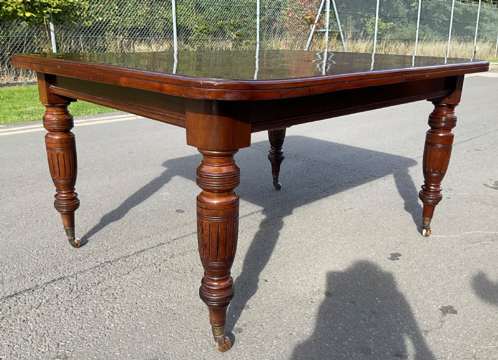 A long Victorian mahogany extending dining table with three insert leaves, rounded corners, and turned legs with brass castors. View X