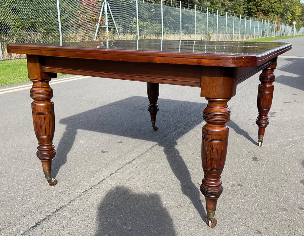 A long Victorian mahogany extending dining table with three insert leaves, rounded corners, and turned legs with brass castors. View XI