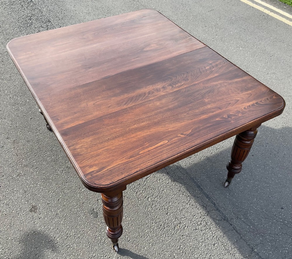 A long Victorian mahogany extending dining table with three insert leaves, rounded corners, and turned legs with brass castors. View XII