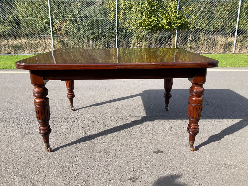 A long Victorian mahogany extending dining table with three insert leaves, rounded corners, and turned legs with brass castors. View XV