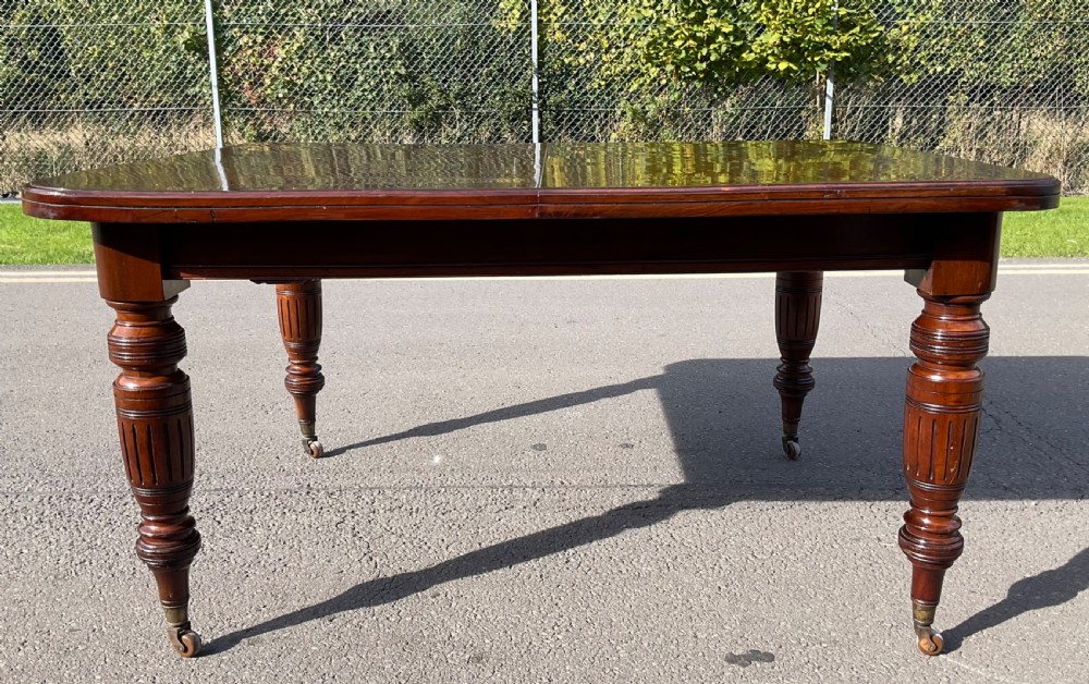 A long Victorian mahogany extending dining table with three insert leaves, rounded corners, and turned legs with brass castors. View XVI