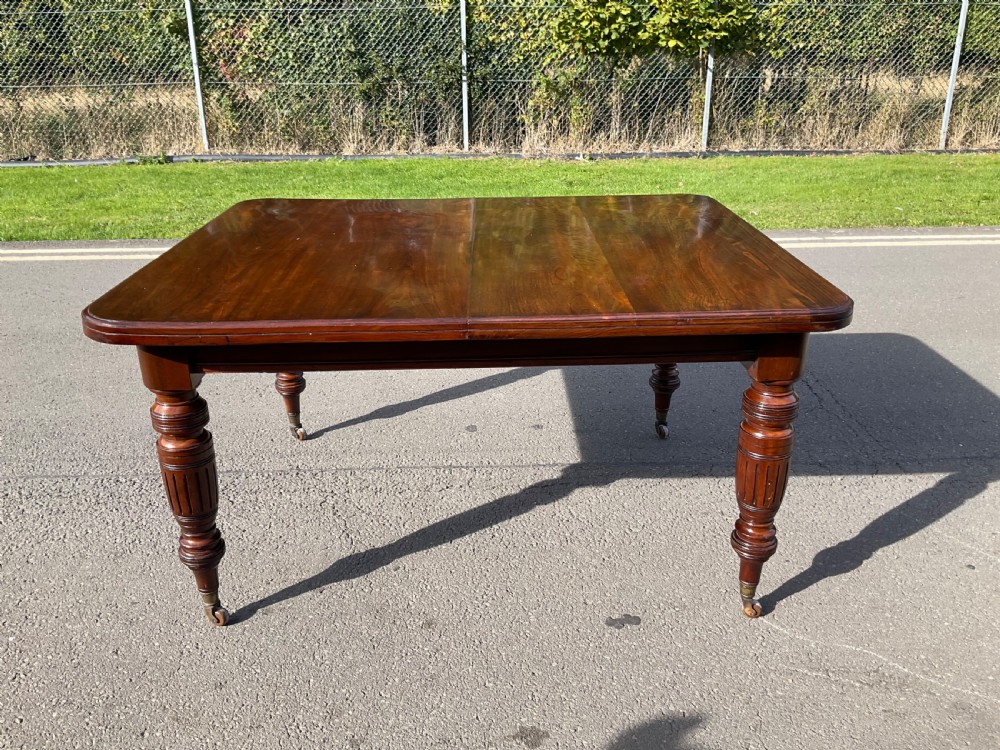 A long Victorian mahogany extending dining table with three insert leaves, rounded corners, and turned legs with brass castors. View XVII