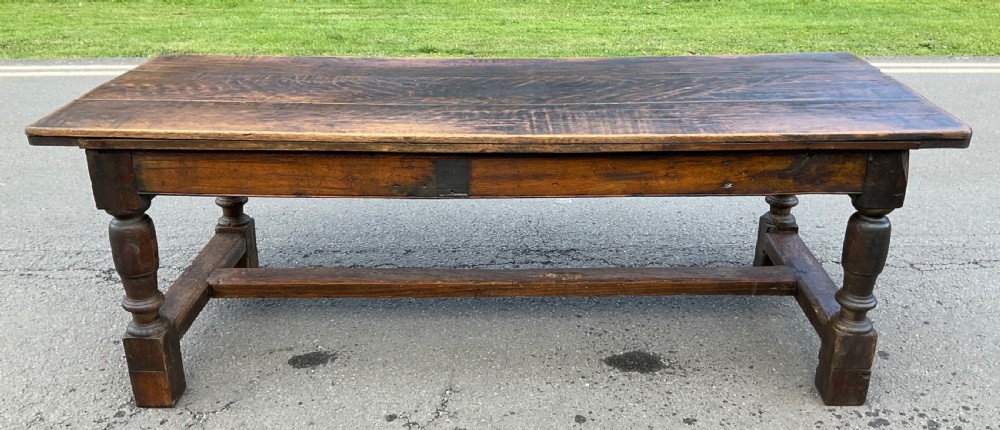 A rectangular antique oak refectory dining table featuring a thick wooden top, turned legs, and a low H-stretcher base.