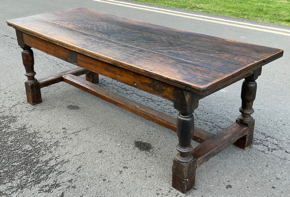 A rectangular antique oak refectory dining table featuring a thick wooden top, turned legs, and a low H-stretcher base. View V