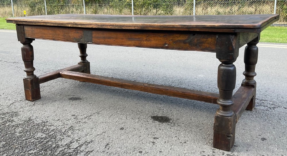 A rectangular antique oak refectory dining table featuring a thick wooden top, turned legs, and a low H-stretcher base. View IX
