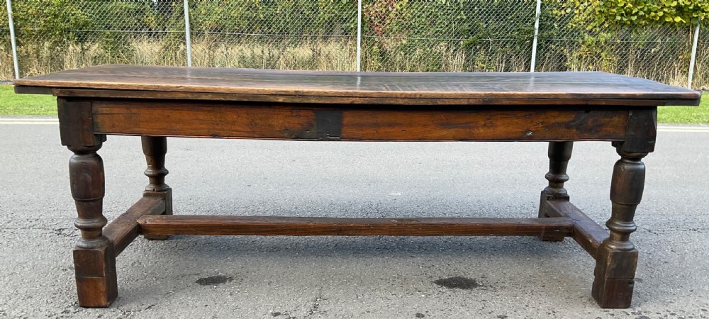 A rectangular antique oak refectory dining table featuring a thick wooden top, turned legs, and a low H-stretcher base. View X