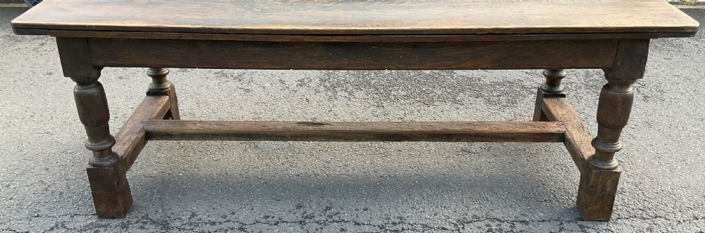 A rectangular antique oak refectory dining table featuring a thick wooden top, turned legs, and a low H-stretcher base. View XII