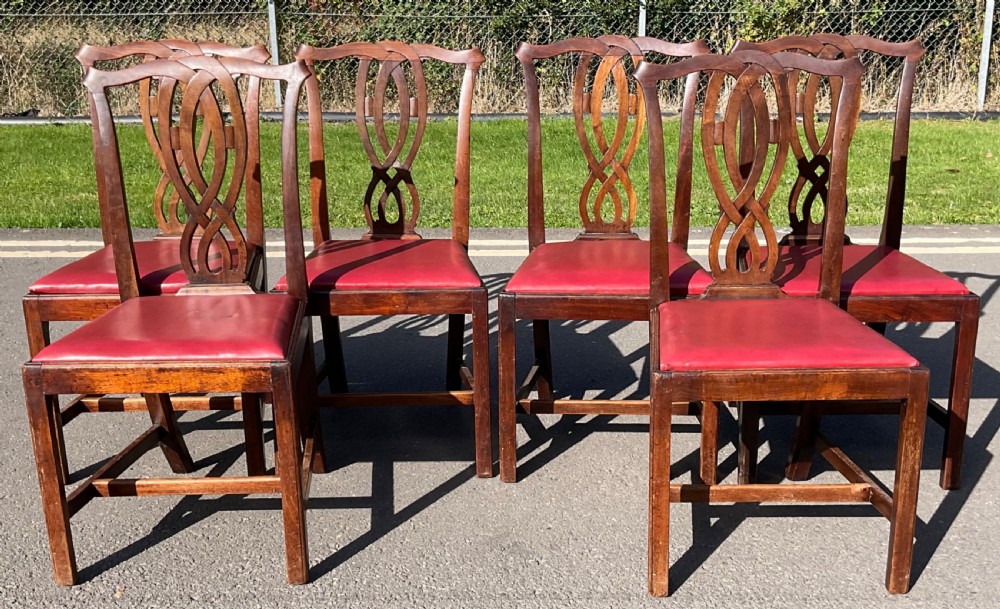 A set of six Georgian mahogany side chairs featuring pierced ribbon-carved back splats, square legs with stretchers, and red leather upholstered seats.