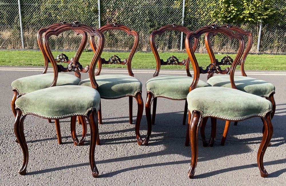 A set of six Victorian walnut balloon back dining chairs featuring carved cresting splats, cabriole front legs, and sage green velvet upholstered seats.