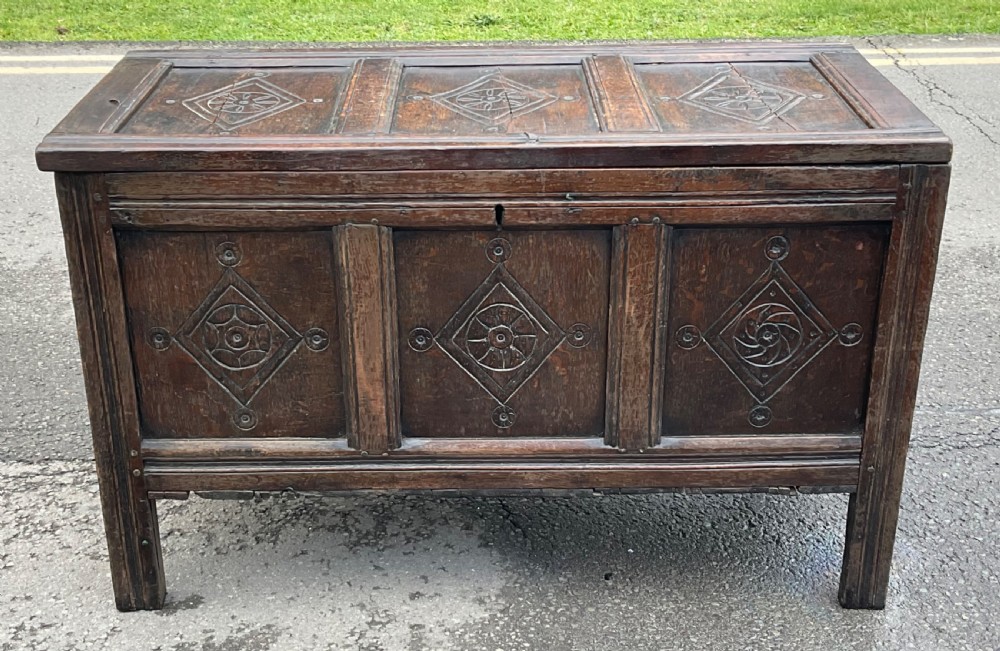 A dark carved oak blanket chest featuring three panelled sections with geometric lozenge carvings.