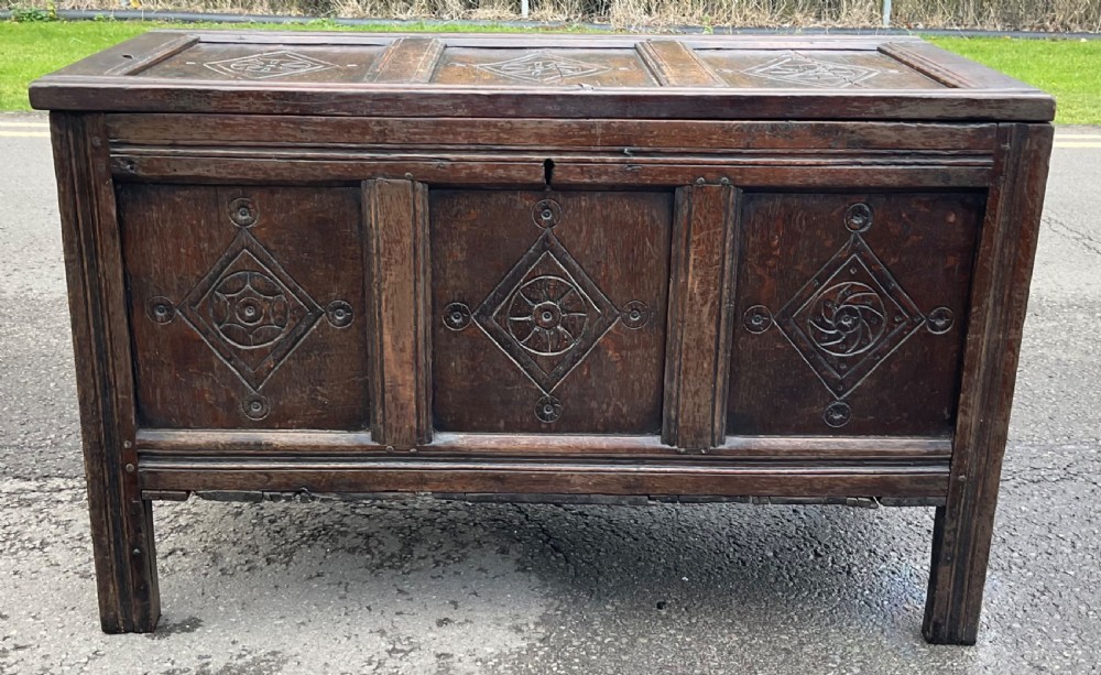A dark carved oak blanket chest featuring three panelled sections with geometric lozenge carvings. View II