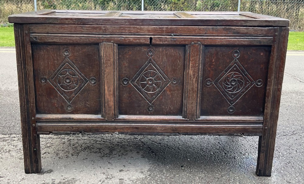 A dark carved oak blanket chest featuring three panelled sections with geometric lozenge carvings. View III