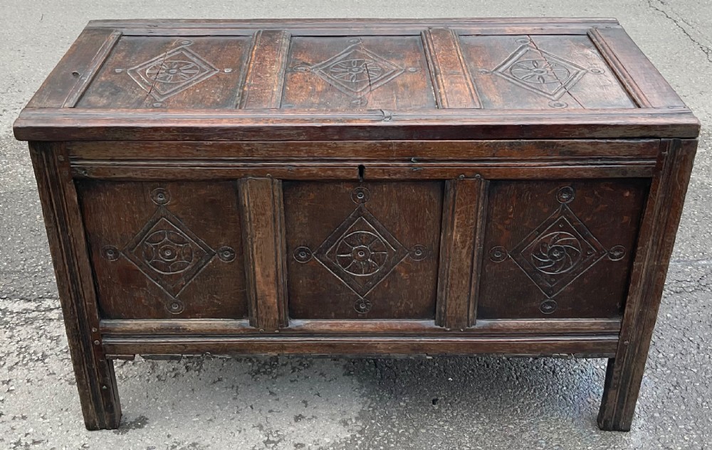 A dark carved oak blanket chest featuring three panelled sections with geometric lozenge carvings. View V
