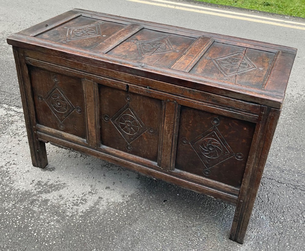 A dark carved oak blanket chest featuring three panelled sections with geometric lozenge carvings. View VI