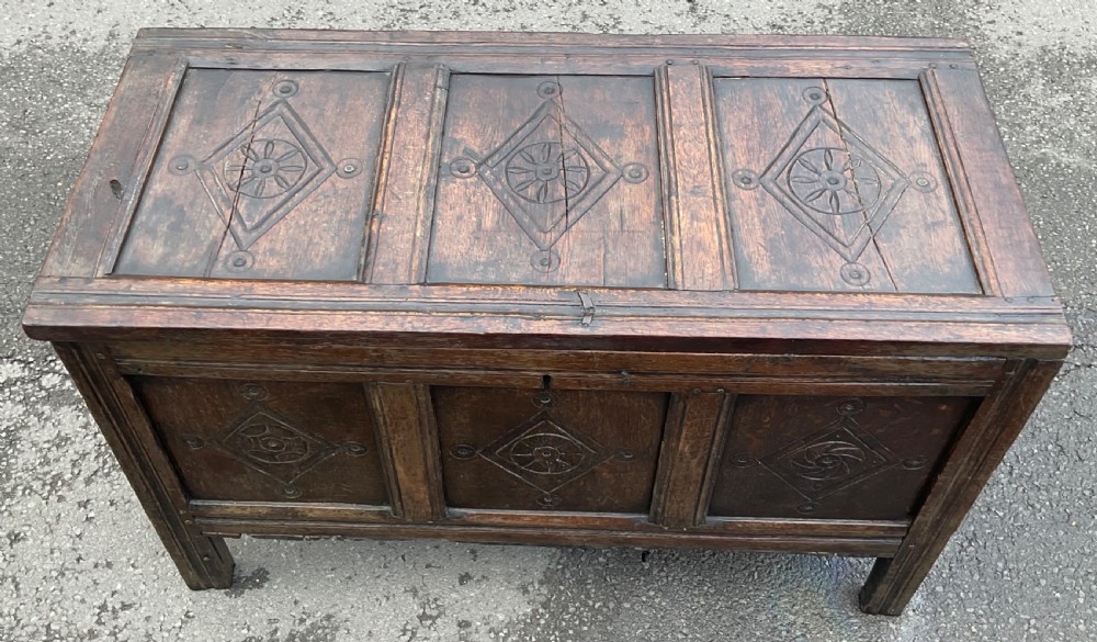 A dark carved oak blanket chest featuring three panelled sections with geometric lozenge carvings. View IX