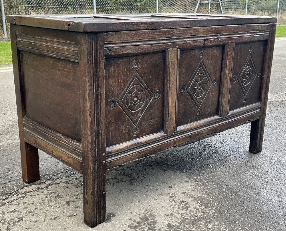 A dark carved oak blanket chest featuring three panelled sections with geometric lozenge carvings. View XI