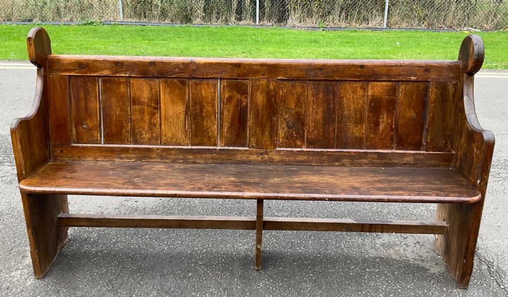 A Victorian pine church pew bench featuring a panelled backrest, shaped side ends with rounded finials, and a warm aged finish.