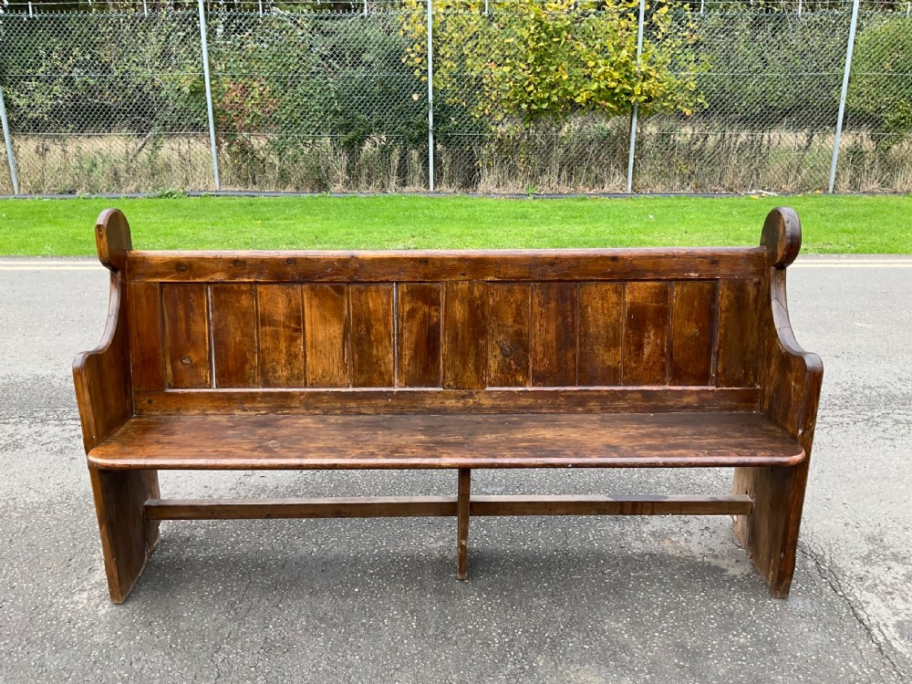 A Victorian pine church pew bench featuring a panelled backrest, shaped side ends with rounded finials, and a warm aged finish. View VI