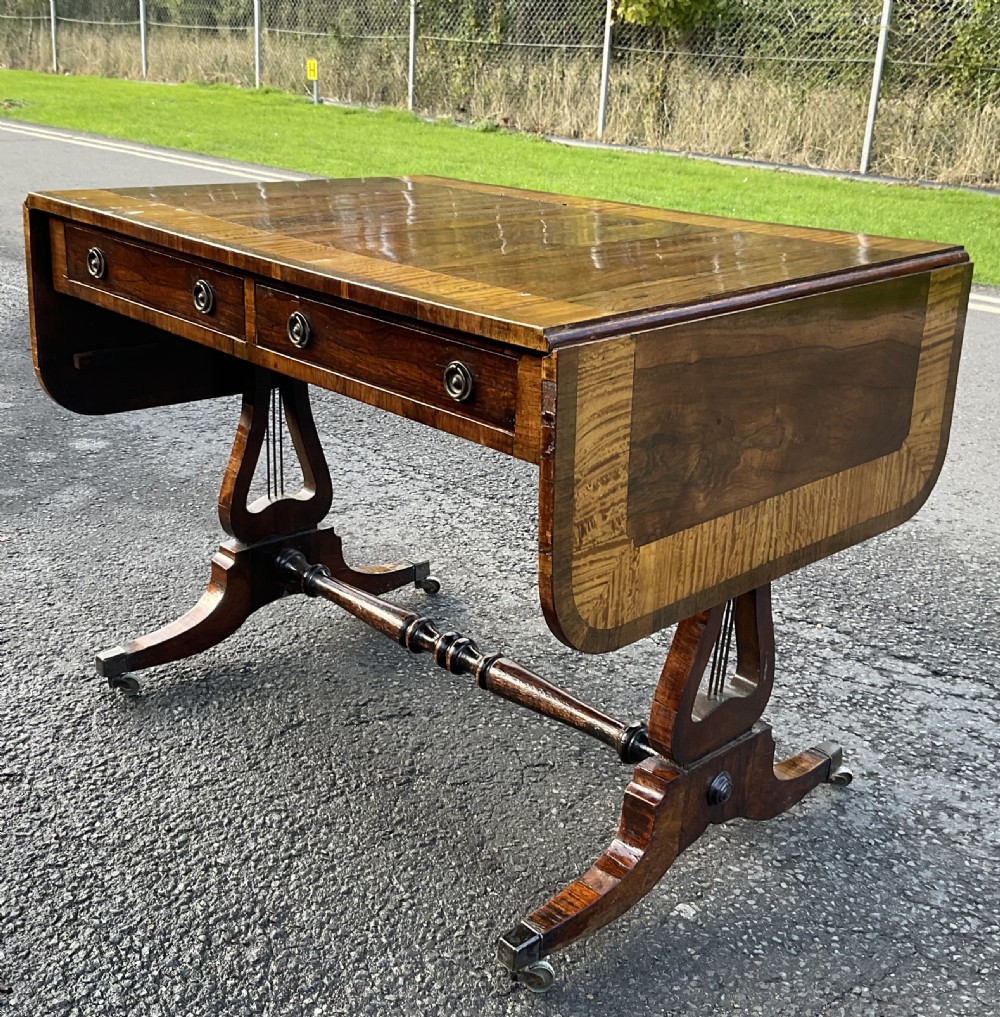 A Georgian walnut drop-leaf sofa table with crossbanded top inlay, two frieze drawers with brass ring handles, turned stretcher support, and splayed legs on castors. View III