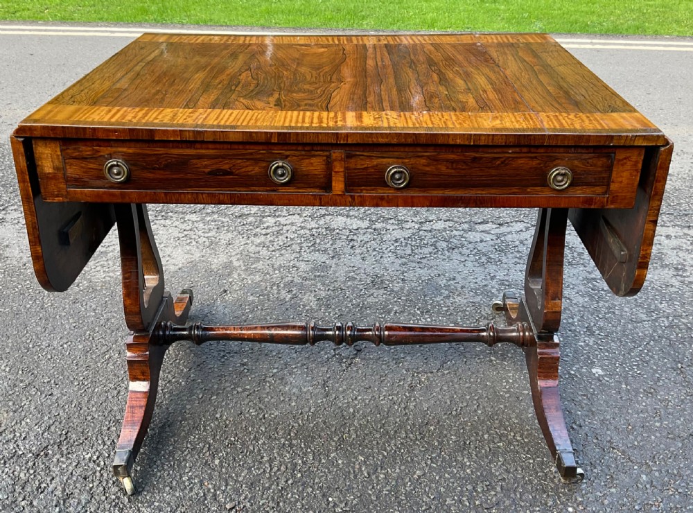 A Georgian walnut drop-leaf sofa table with crossbanded top inlay, two frieze drawers with brass ring handles, turned stretcher support, and splayed legs on castors. View VII