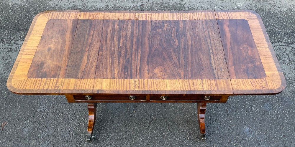 A Georgian walnut drop-leaf sofa table with crossbanded top inlay, two frieze drawers with brass ring handles, turned stretcher support, and splayed legs on castors. View XI