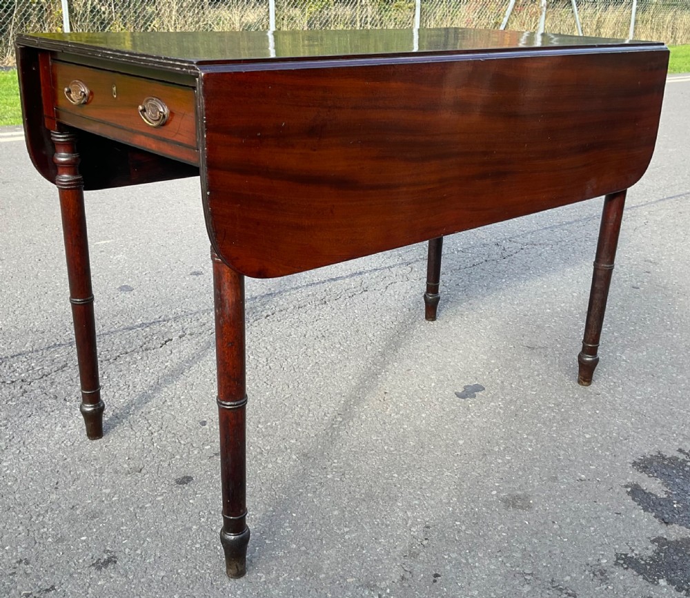 A Georgian mahogany Pembroke table featuring two drop-leaf sides, a single frieze drawer with brass handles, and four turned legs.