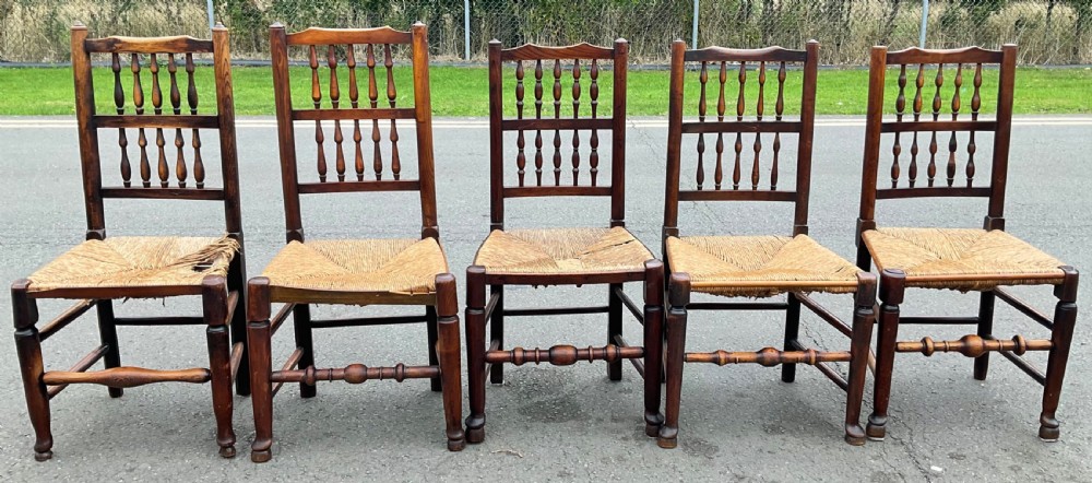 A set of five antique elm Lancashire spindleback dining chairs featuring double-tiered turned back spindles and woven rush seats.