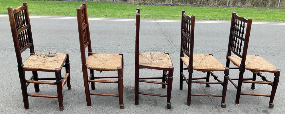 A set of five antique elm Lancashire spindleback dining chairs featuring double-tiered turned back spindles and woven rush seats. View V