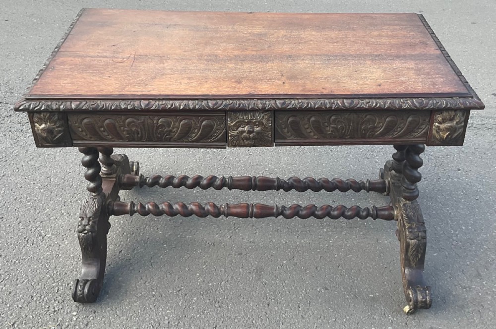 A Victorian carved dark oak writing table with two drawers featuring lion mask carvings, barley twist legs, and twin stretchers. View II