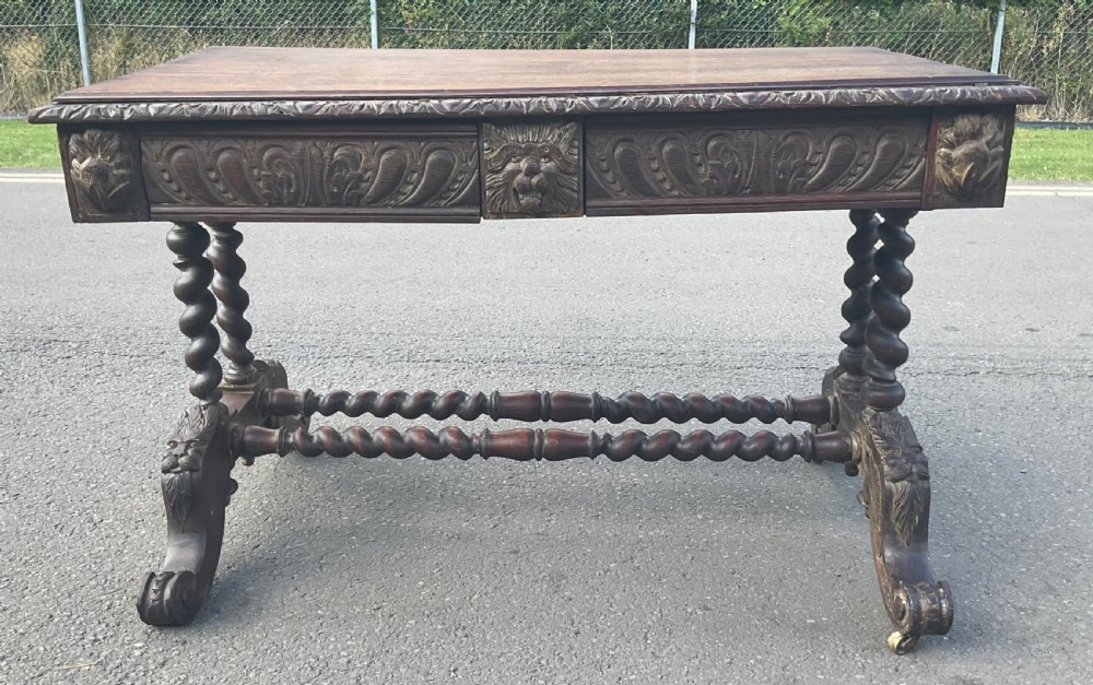 A Victorian carved dark oak writing table with two drawers featuring lion mask carvings, barley twist legs, and twin stretchers. View III