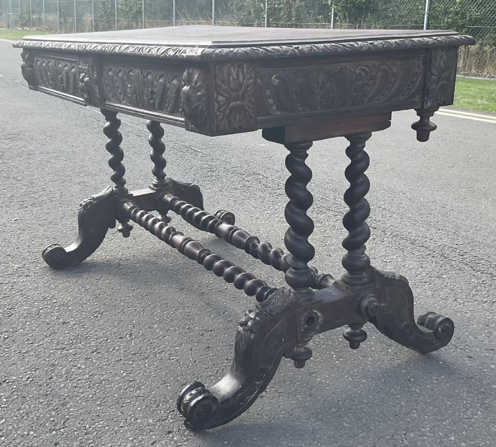 A Victorian carved dark oak writing table with two drawers featuring lion mask carvings, barley twist legs, and twin stretchers. View VI