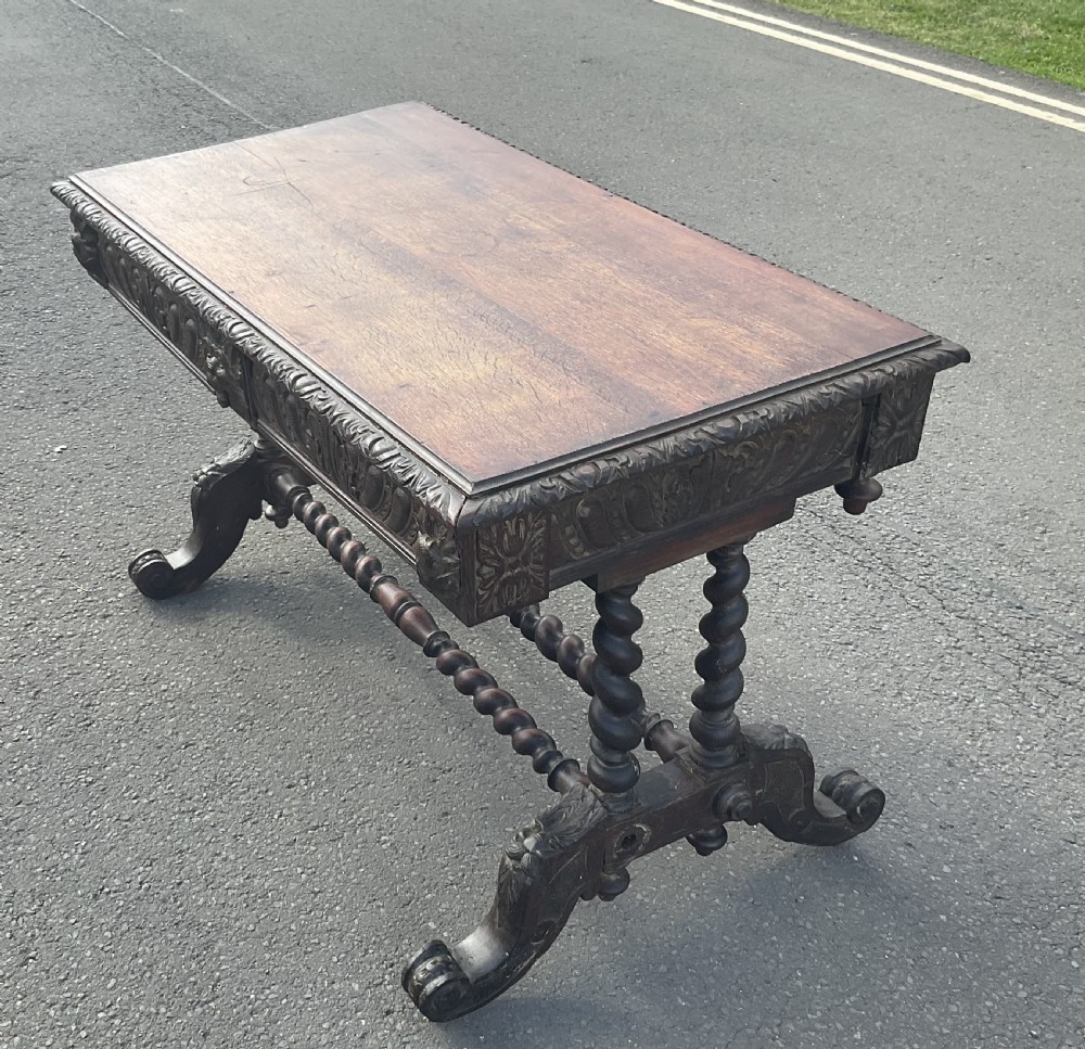 A Victorian carved dark oak writing table with two drawers featuring lion mask carvings, barley twist legs, and twin stretchers. View VII