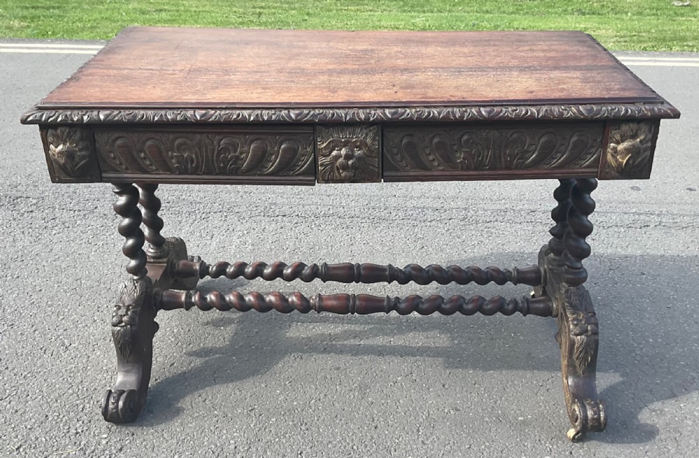 A Victorian carved dark oak writing table with two drawers featuring lion mask carvings, barley twist legs, and twin stretchers. View VIII