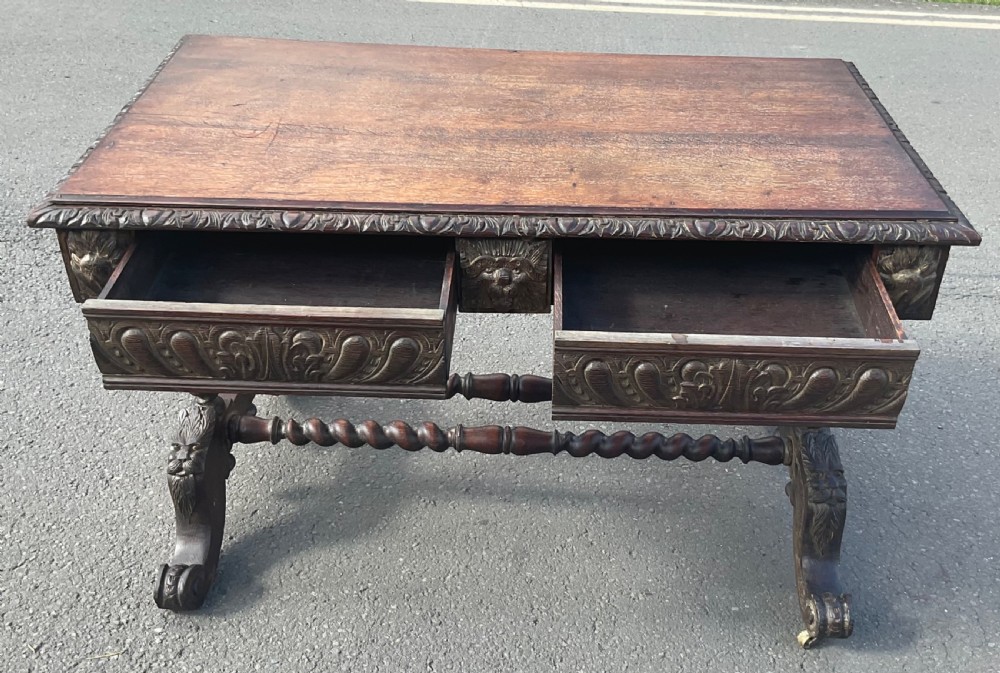 A Victorian carved dark oak writing table with two drawers featuring lion mask carvings, barley twist legs, and twin stretchers. View IX