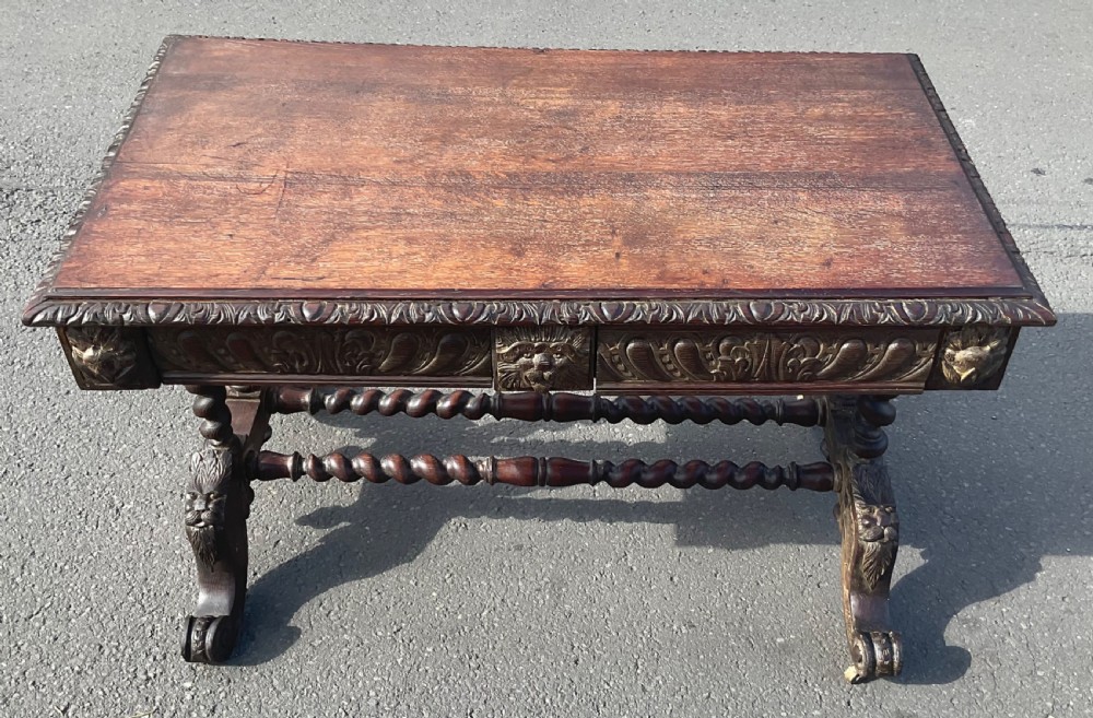 A Victorian carved dark oak writing table with two drawers featuring lion mask carvings, barley twist legs, and twin stretchers. View X