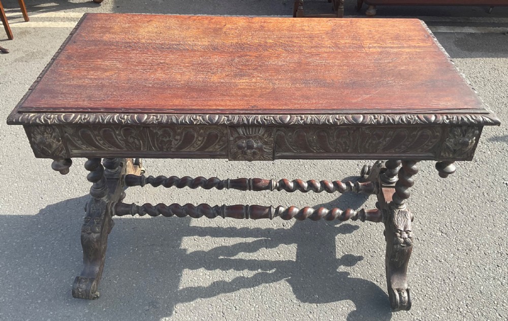 A Victorian carved dark oak writing table with two drawers featuring lion mask carvings, barley twist legs, and twin stretchers. View XI
