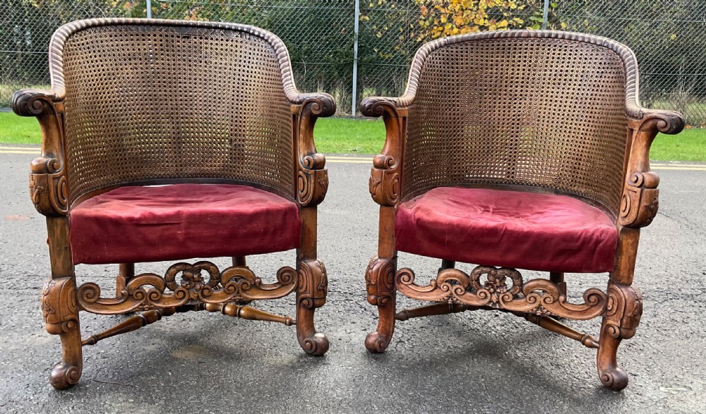 A pair of carved walnut armchairs featuring woven cane backrests, scrollwork aprons, and red velvet seat cushions.