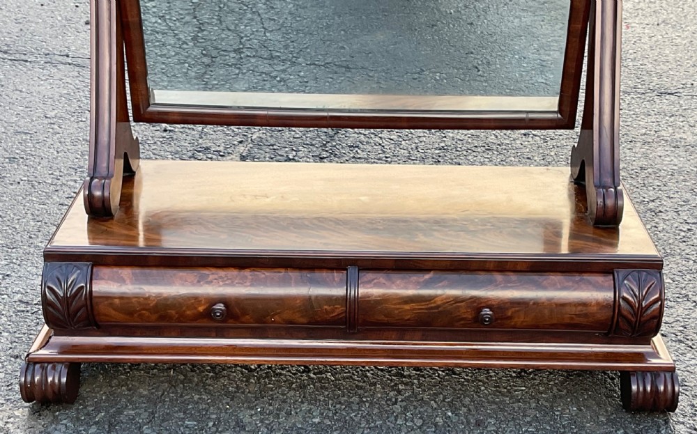 A mahogany toilet mirror featuring a rectangular swivelling glass frame supported by turned uprights on a plinth base with a frieze drawer and carved feet. View IV
