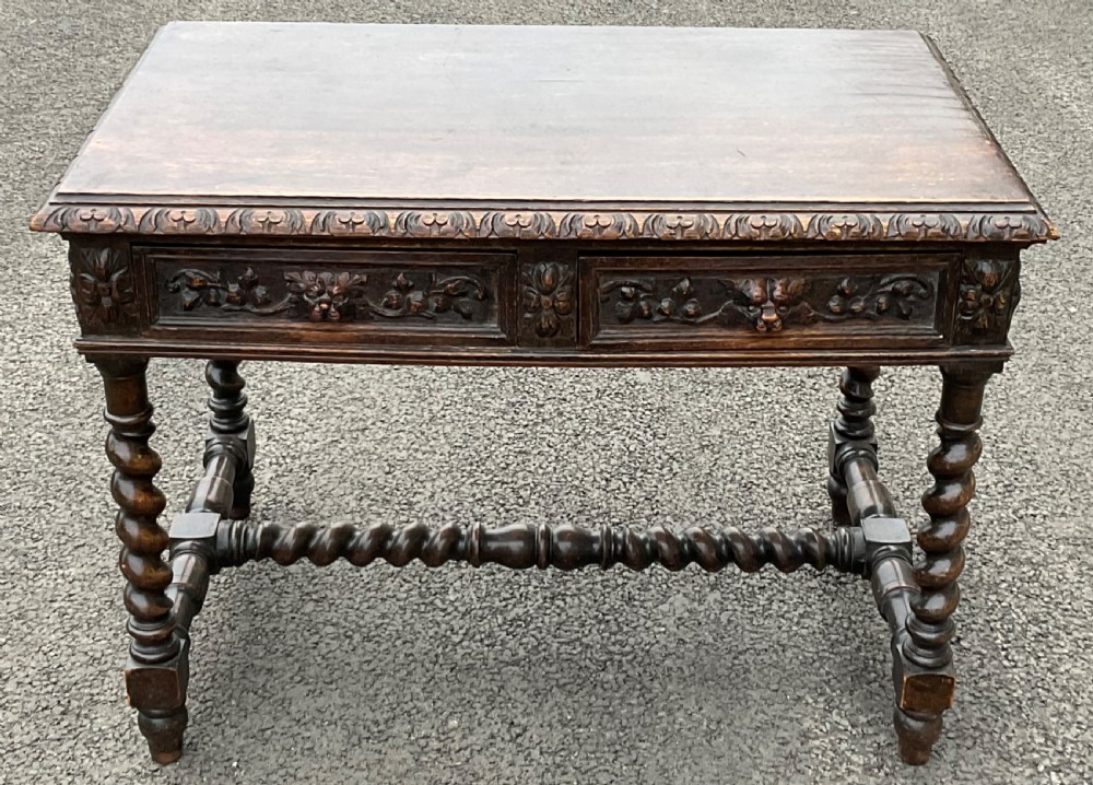 A dark oak Victorian writing table with relief-carved drawer fronts and barley twist legs connected by a matching stretcher.