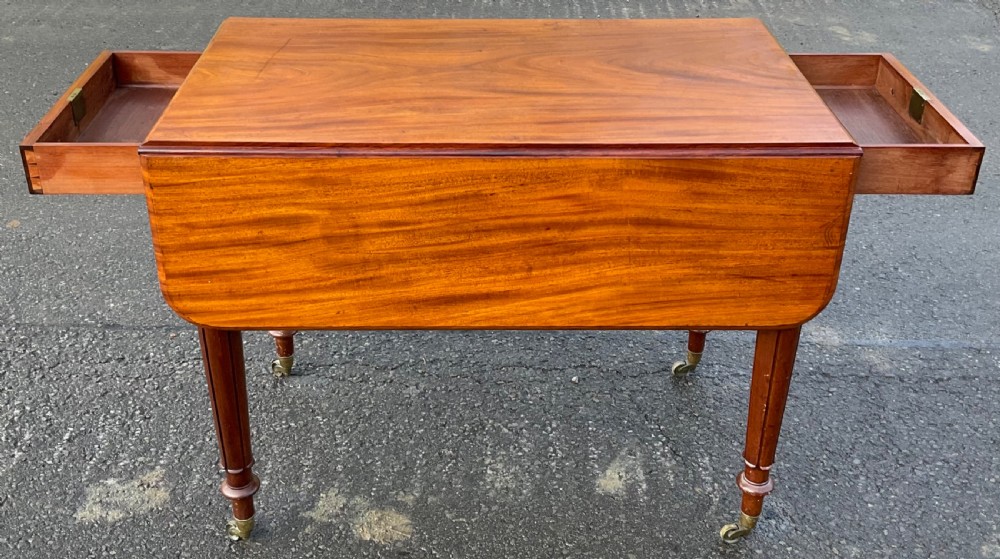 A Victorian mahogany Pembroke table featuring two drop leaves, a single frieze drawer with wooden knobs, turned reeded legs, and brass castors. View II
