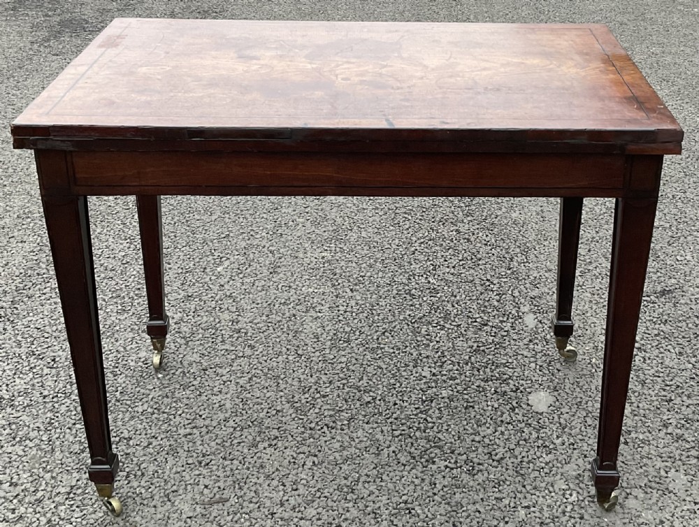 A Georgian mahogany side table featuring an inlaid rectangular top, straight square tapered legs, and original brass castors.