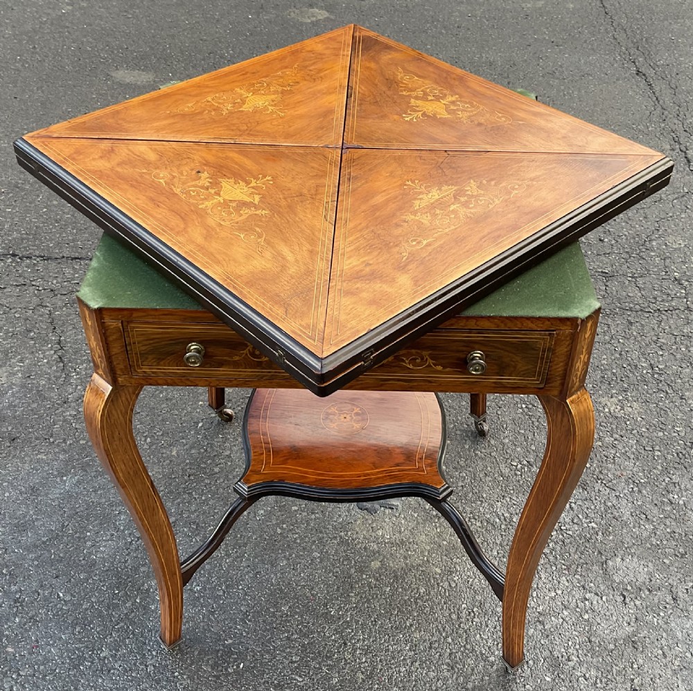 An Edwardian inlaid mahogany envelope card table featuring triangular fold-out top sections with marquetry urn motifs, a single frieze drawer, cabriole legs, and a shaped undertier. View V