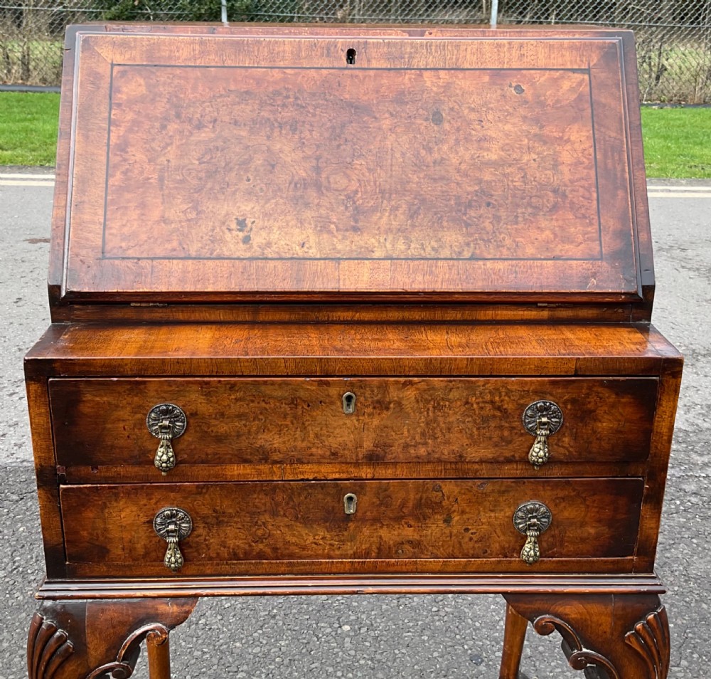 A small Queen Anne style walnut writing bureau featuring a slant-front flap, two drawers with brass handles, and cabriole legs with pad feet. View IV