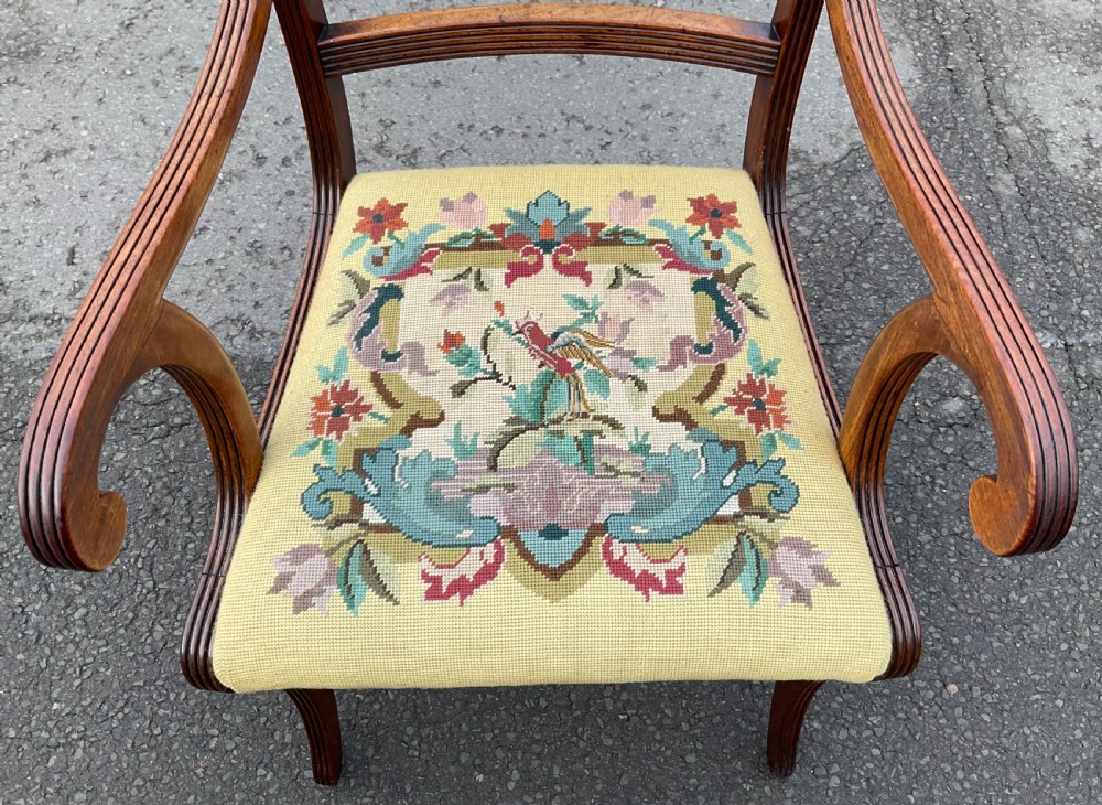 A Regency mahogany carver armchair featuring reeded scrolling arms, reeded curved legs, a tablet back rail, and a yellow needlepoint upholstered seat depicting floral and bird motifs. View II