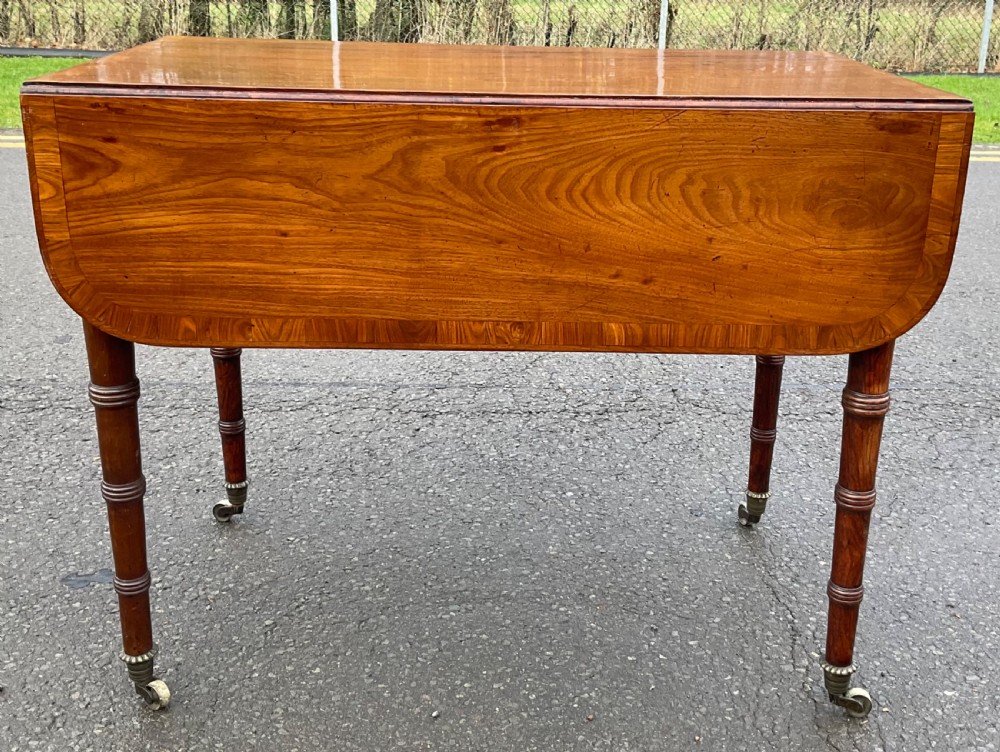 A Georgian mahogany Pembroke table featuring two hinged drop leaves, a crossbanded timber border, ring-turned legs, and brass castors.