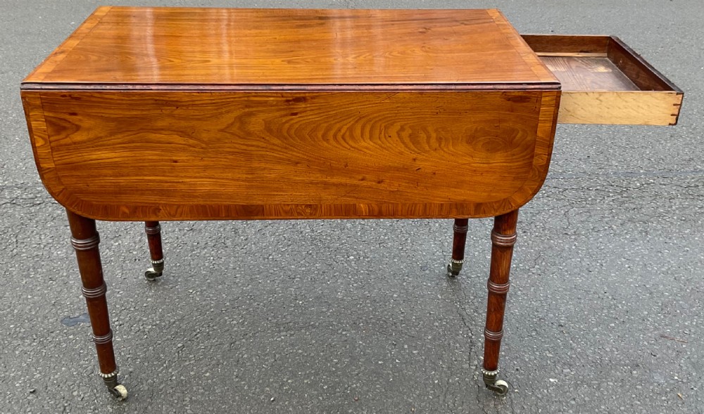 A Georgian mahogany Pembroke table featuring two hinged drop leaves, a crossbanded timber border, ring-turned legs, and brass castors. View III