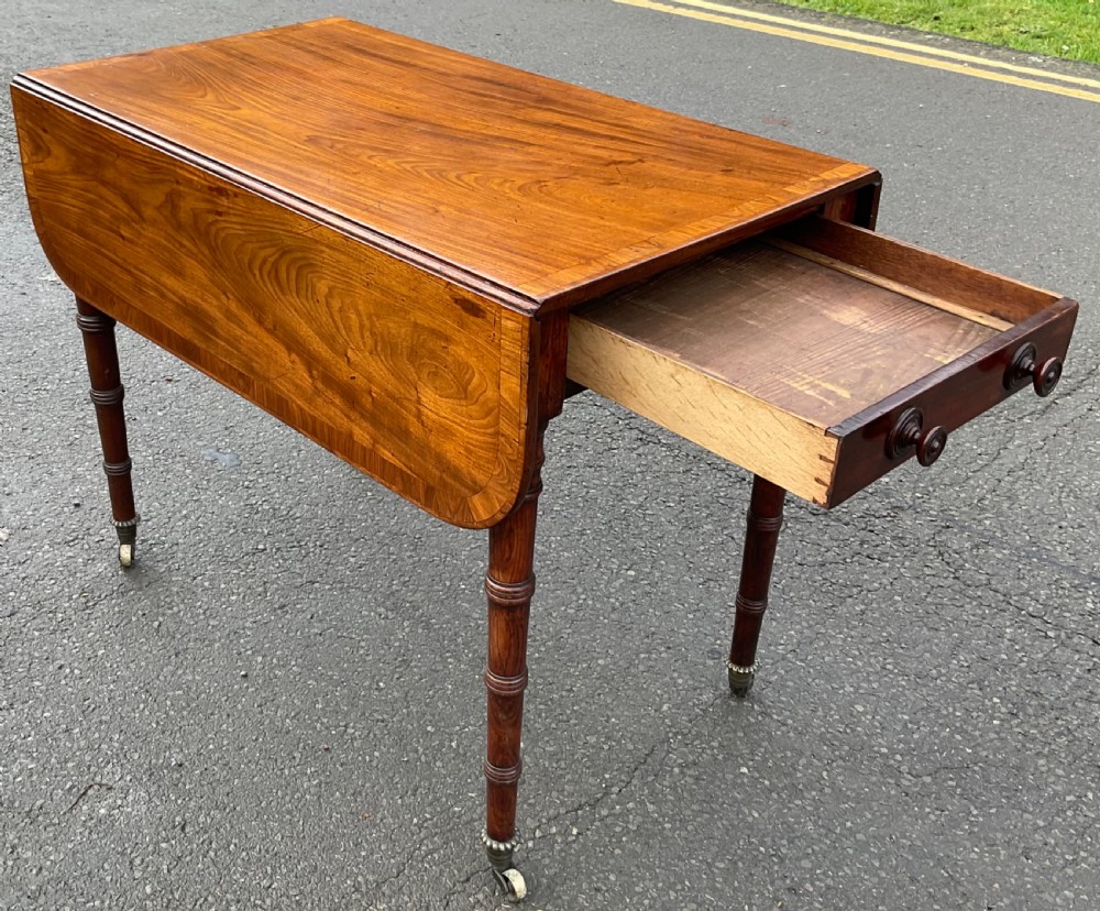 A Georgian mahogany Pembroke table featuring two hinged drop leaves, a crossbanded timber border, ring-turned legs, and brass castors. View V