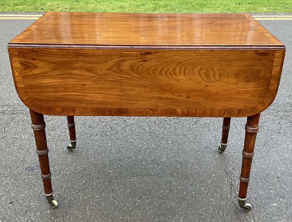 A Georgian mahogany Pembroke table featuring two hinged drop leaves, a crossbanded timber border, ring-turned legs, and brass castors. View VI