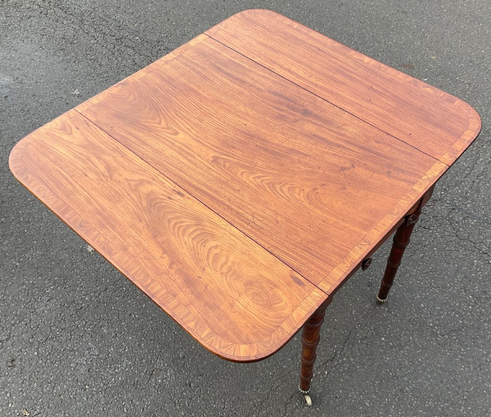 A Georgian mahogany Pembroke table featuring two hinged drop leaves, a crossbanded timber border, ring-turned legs, and brass castors. View VII