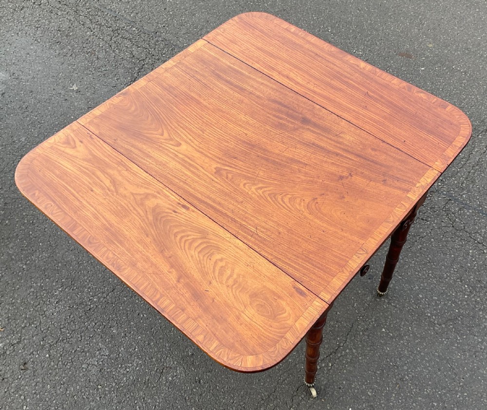 A Georgian mahogany Pembroke table featuring two hinged drop leaves, a crossbanded timber border, ring-turned legs, and brass castors. View VIII